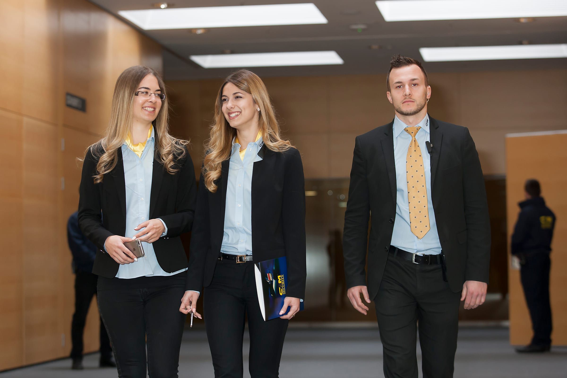 Zwei Hostessen und ein Host in CAM-Outfits gehen durch einen Kongressgang